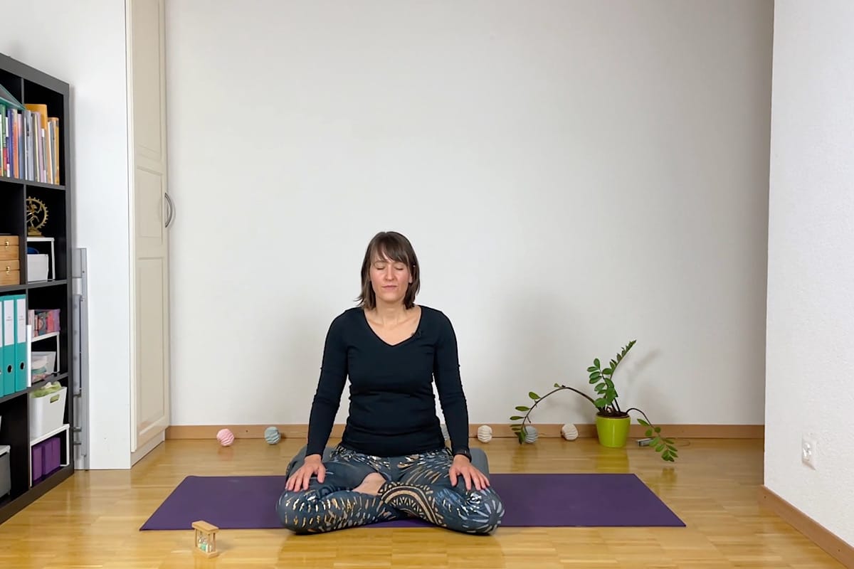 Eine Person sitzt im Schneidersitz auf einer lila Yogamatte in einem ruhigen Raum und praktiziert Yoga zum Einschlafen.