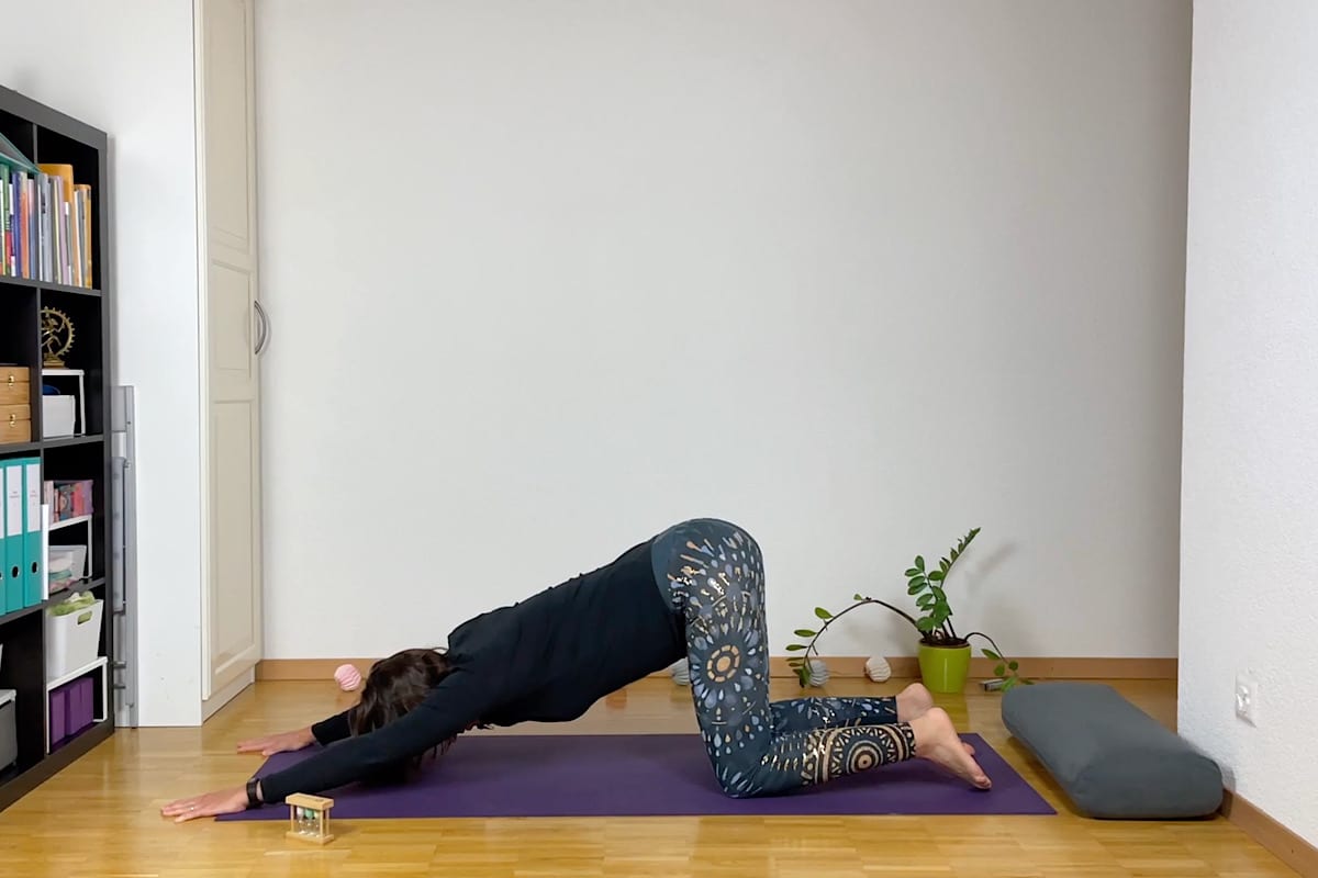 Eine Person macht Yoga zum Einschlafen. Sie liegt auf einer lila Matte und entspannt sich in einer Vorwärtsdehnung mit ausgestreckten Armen, die Stirn ruht sanft.