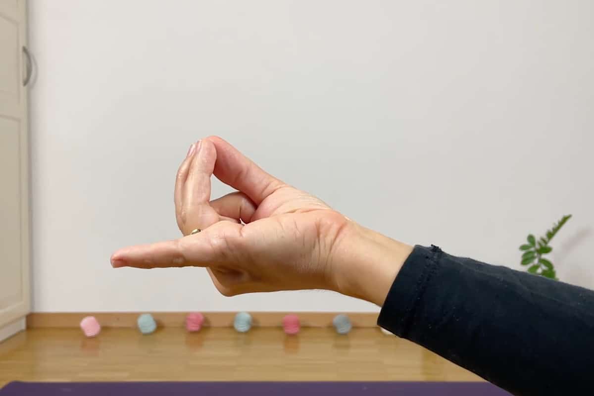 Eine Hand macht eine Mudra-Geste vor einem schlichten Hintergrund, die Ruhe ausstrahlt, ideal für Yoga zum Einschlafen, mit bunten Bällen auf dem Boden und einer kleinen Pflanze in der Ecke.