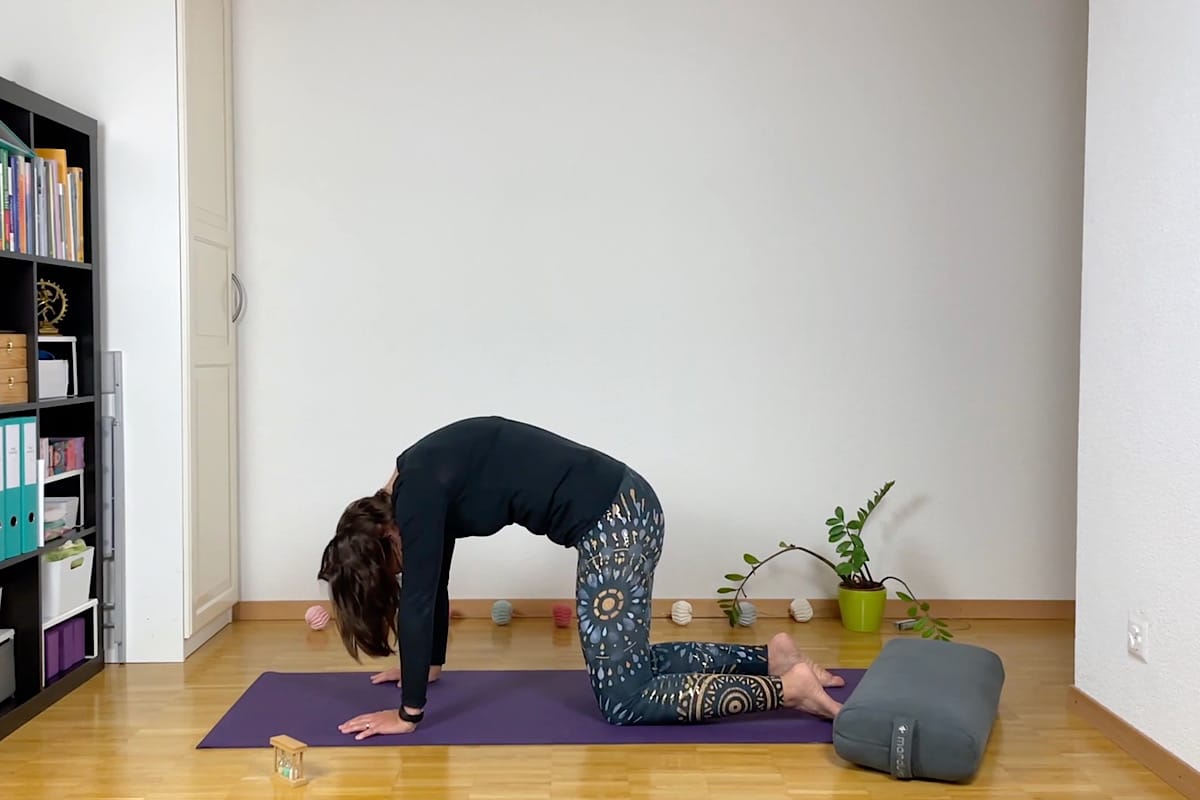 Eine Person macht drinnen auf einer lila Matte die Yogapose Katze-Kuh.