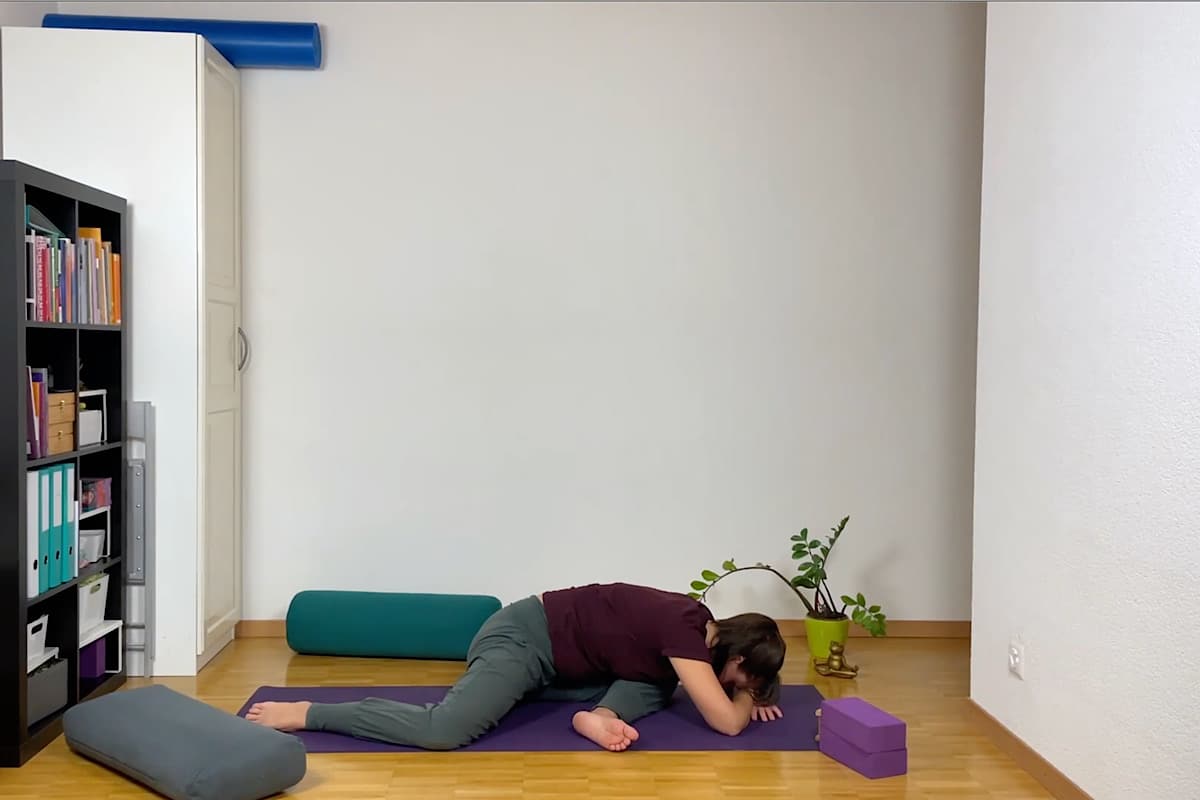 Eine Person macht Yin Yoga. Sie befindet sich in einer tiefen Streckung, wobei ein Bein nach vorne gebeugt und das andere nach hinten gestreckt ist.