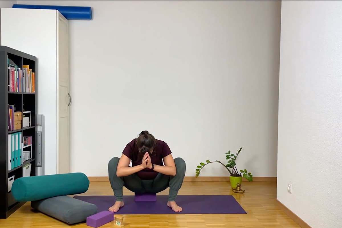 Eine Person praktiziert Yin Yoga. Sie sitzt in einer Hockstellung auf einer Yogamatte und hat die Hände in einer Gebetshaltung.
